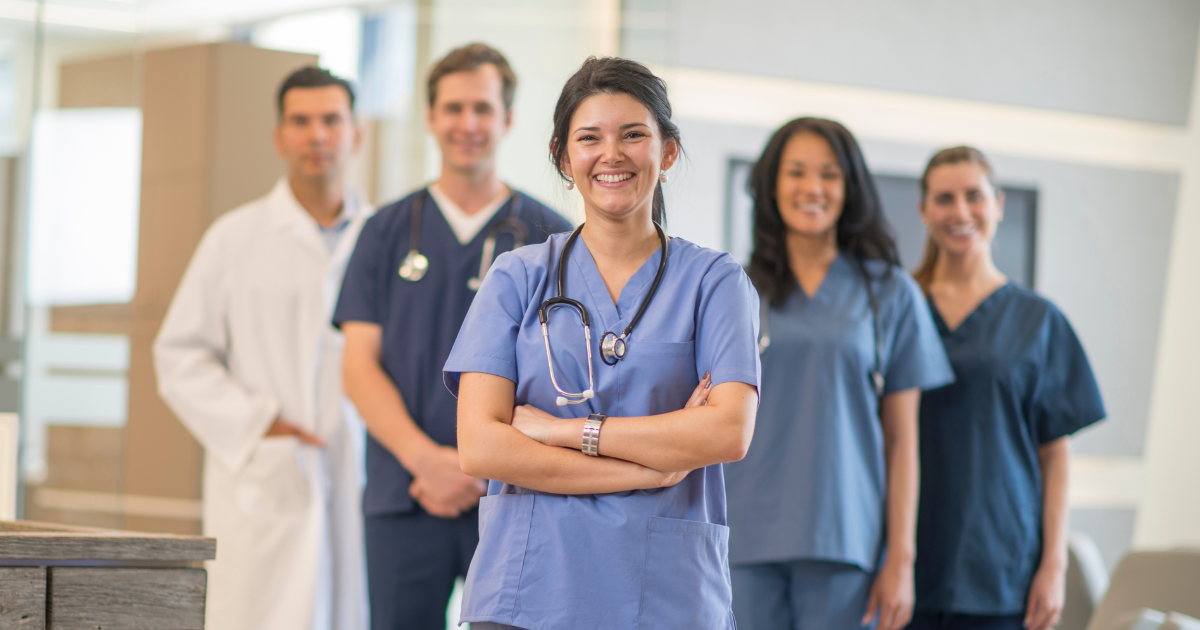 A smiling group of nurses and other healthcare professionals standing together, presenting teamwork for Nurses Week.