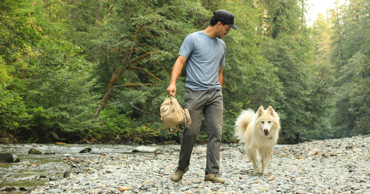 Person walking with a dog along a peaceful river, practicing healthy coping skills and self-care in addiction recovery.