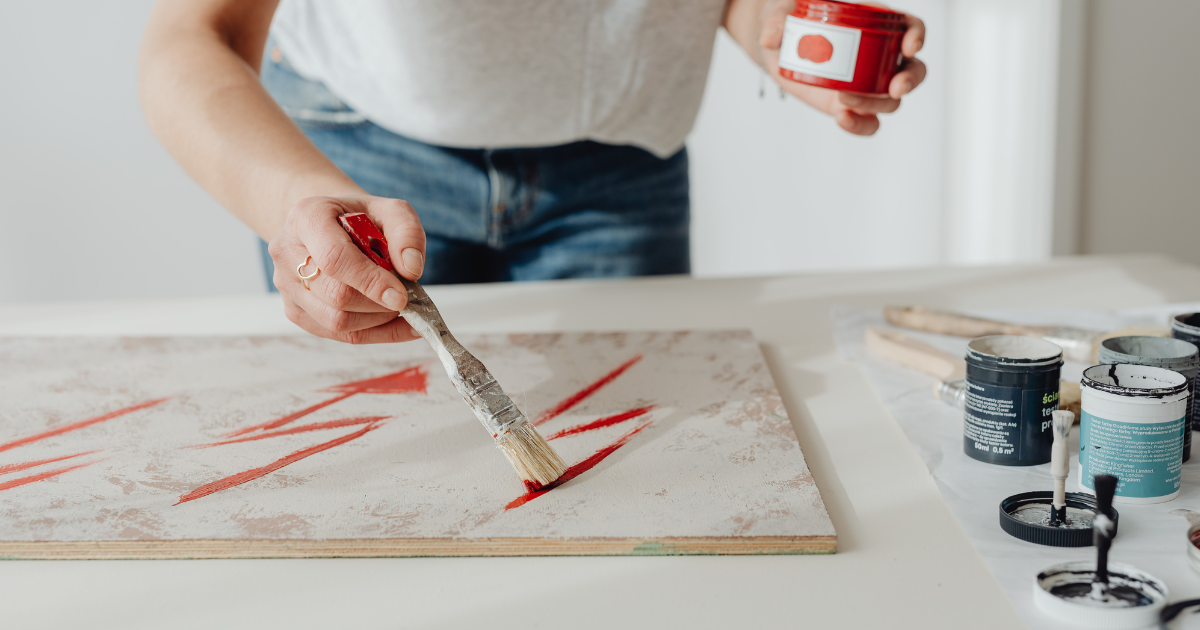 A person painting abstract red lines on canvas, using creative expression as a healthy distraction and coping skill in substance use recovery.