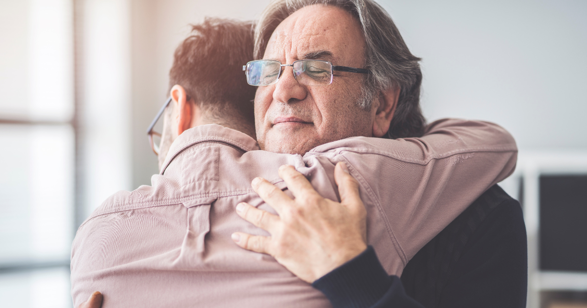 Older man embracing a younger man in a supportive hug, symbolizing family support and compassion in addiction recovery.