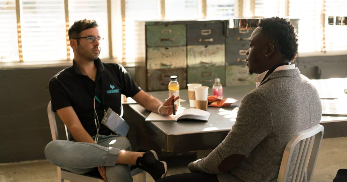 A counselor meeting with a patient in a relaxed, sunlit room. They are seated across from each other at a table with notebooks and drinks, symbolizing support and open communication in addiction recovery.