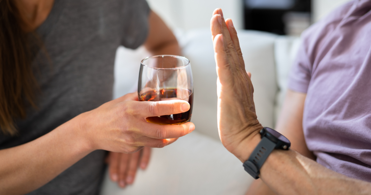 Individual raising a hand to decline an alcoholic drink at a social gathering, representing setting boundaries, handling social pressure and protecting recovery during holidays in recovery.