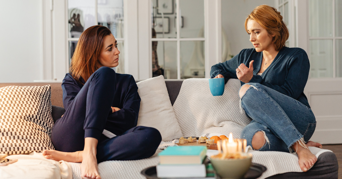 Two women sitting together and talking on a couch, representing recovery support, connection and leaning on a trusted friend during celebrations and holidays in recovery.