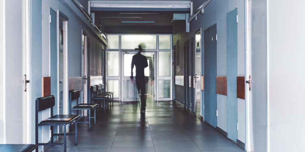 Man walking through modern healthcare facility corridor with blue walls and clinical seating areas.