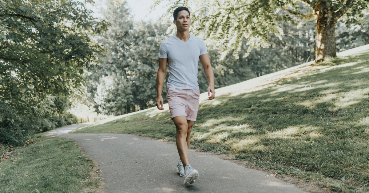Man walking on a paved path in a park, practicing self-care and stress management as part of his recovery journey during the holiday season.