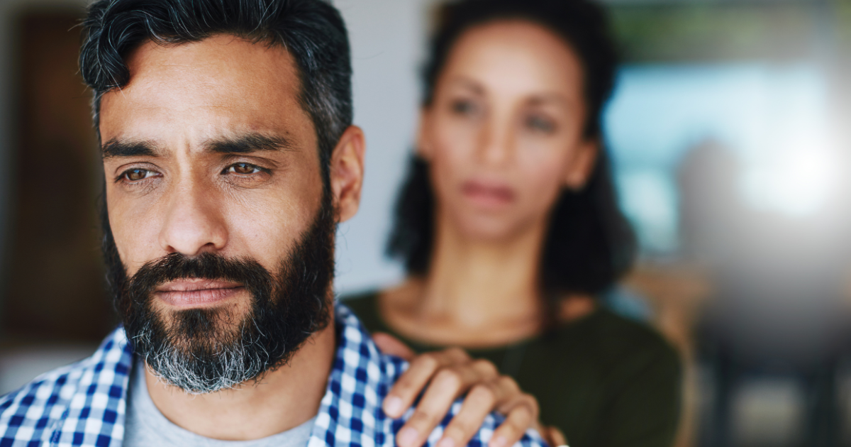 A man with a serious expression, supported by a woman, symbolizing the challenges and hope in overcoming opioid use disorder and seeking recovery.