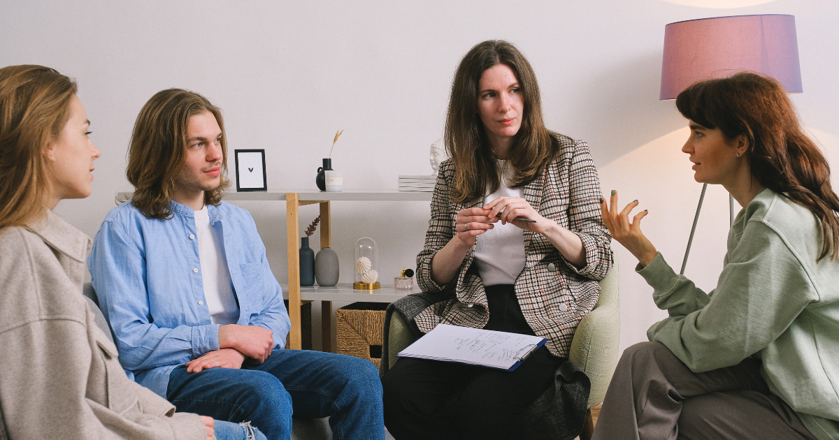 A group counseling session with a substance use counselor and three individuals sitting in a circle, actively engaged in conversation in a calm, supportive setting.