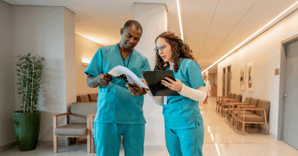Two healthcare nurses reviewing patient chart in modern medical facility hallway during shift.