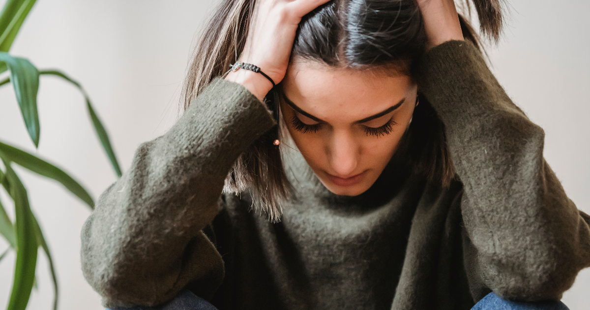 Woman sitting with her head in her hands, reflecting the emotional toll of stigma and misconceptions surrounding opioid use disorder and treatment.