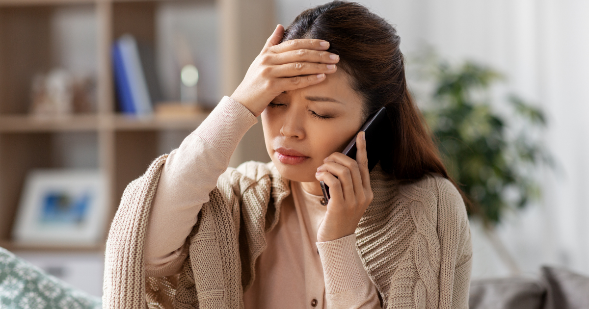 Woman with her hand on her forehead, looking worried while speaking on the phone, demonstrating the potential side effects of Naltrexone and the importance of reaching out for help.