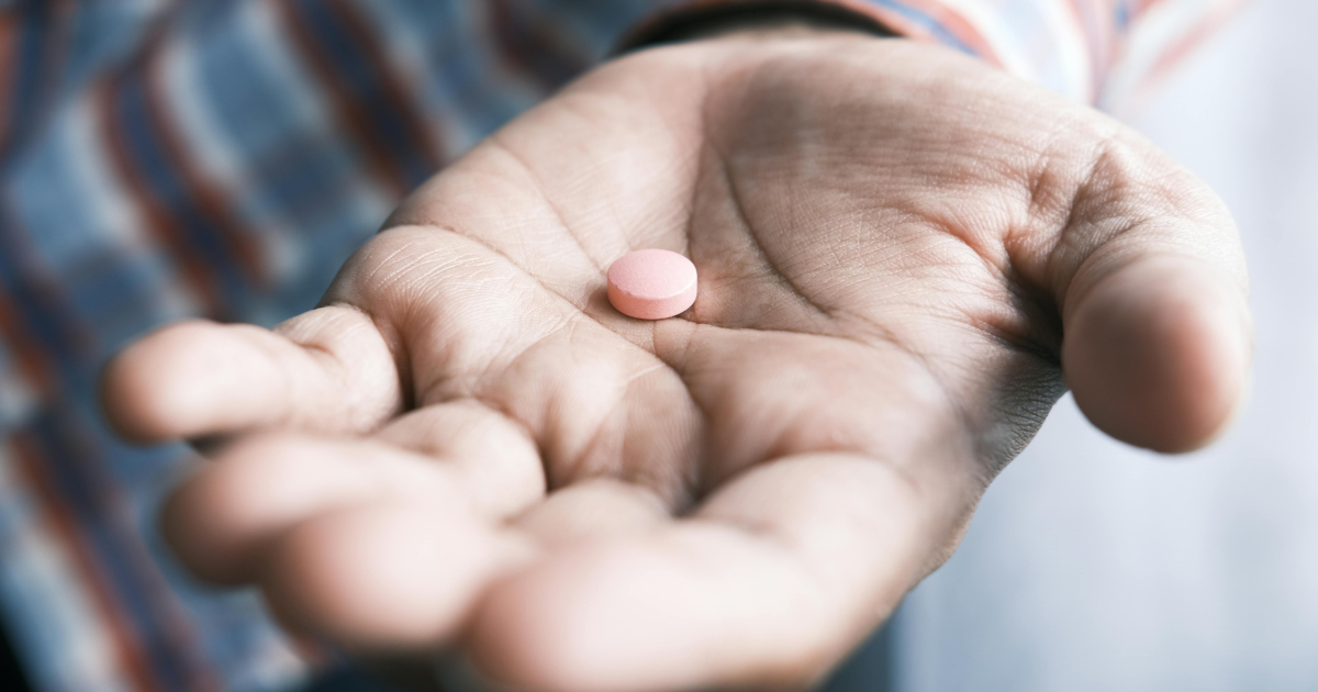 A close-up of a person's hand holding a single pink or orange tablet, symbolizing buprenorphine medication used for opioid use disorder treatment.
