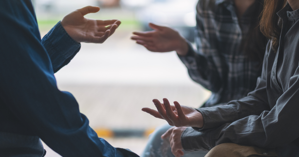 Close-up of a small group in conversation, with hands gesturing as they talk, symbolizing open dialogue and breaking the stigma around addiction.