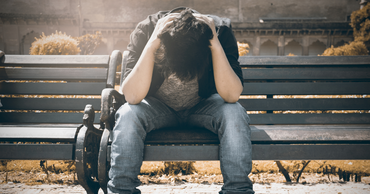 Person sitting alone on a bench with head in hands, representing feelings of shame, isolation and the impact of addiction stigma.