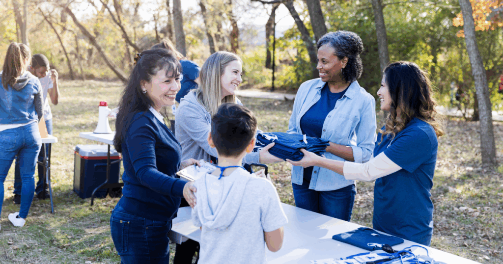 Volunteers distributing blue t-shirts at outdoor community recovery event in park setting.
