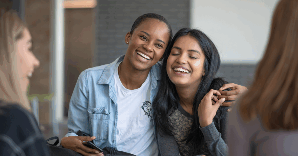 Two young women laughing together while conversing with others in a supportive group setting.