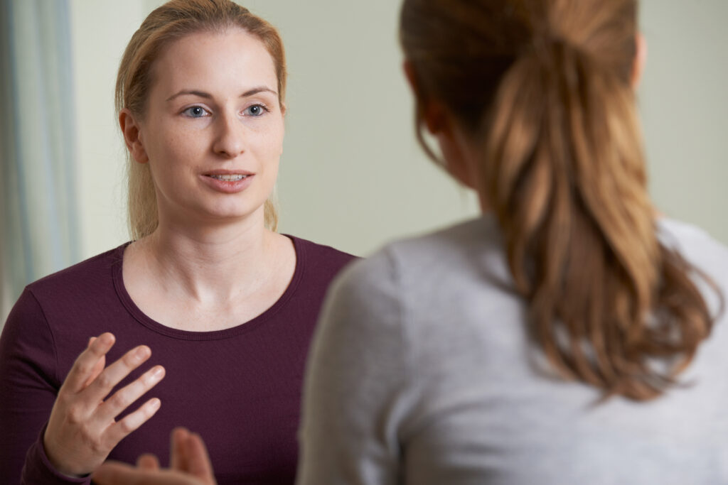 Young woman in maroon shirt speaking with counselor during therapy session discussion.