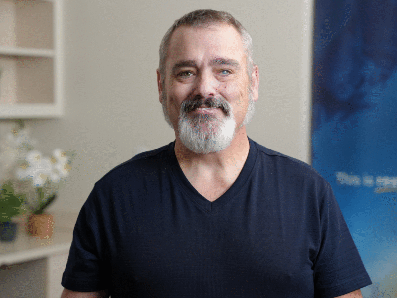 Middle-aged man with gray beard in dark shirt shares recovery story for addiction treatment provider.