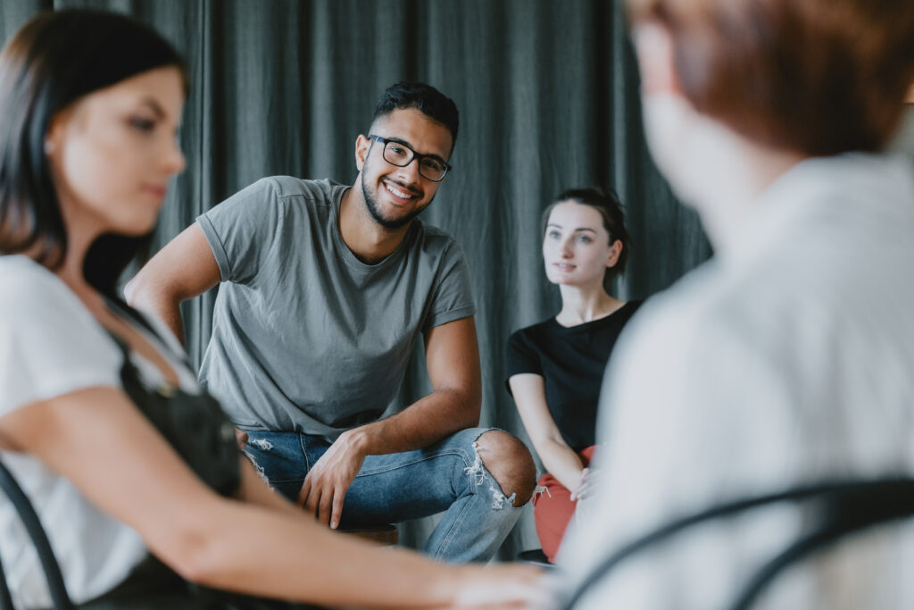 Diverse group of young people sitting together in circle, smiling and engaged in conversation or group discussion.