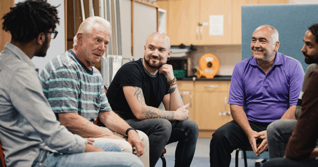 Group of diverse men sitting in circle during substance abuse counseling session indoors.