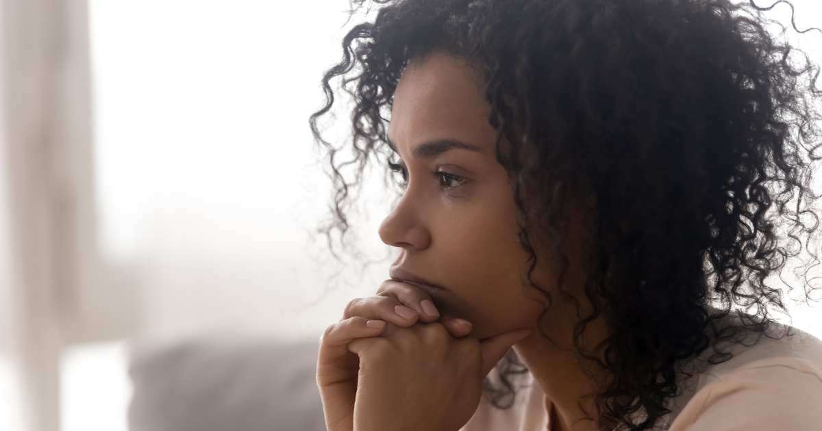 Thoughtful woman with curly hair gazing downward, contemplative expression depicting addiction recovery consideration.