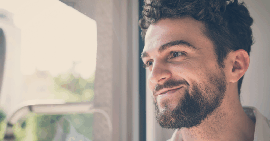 Man gazing thoughtfully out window, contemplative expression suggesting recovery and hope.