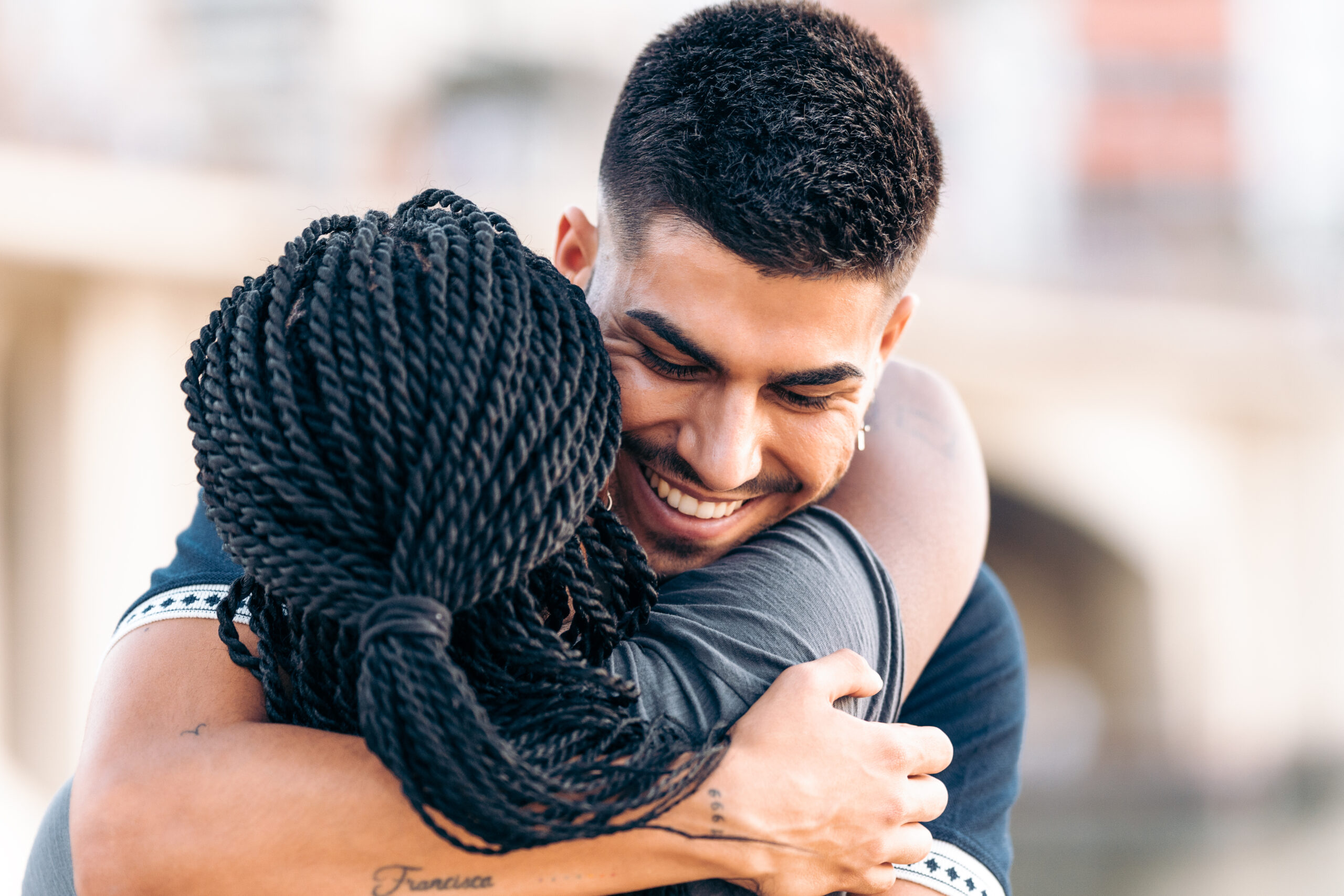 Man and woman embracing outdoors, smiling warmly together in supportive moment.
