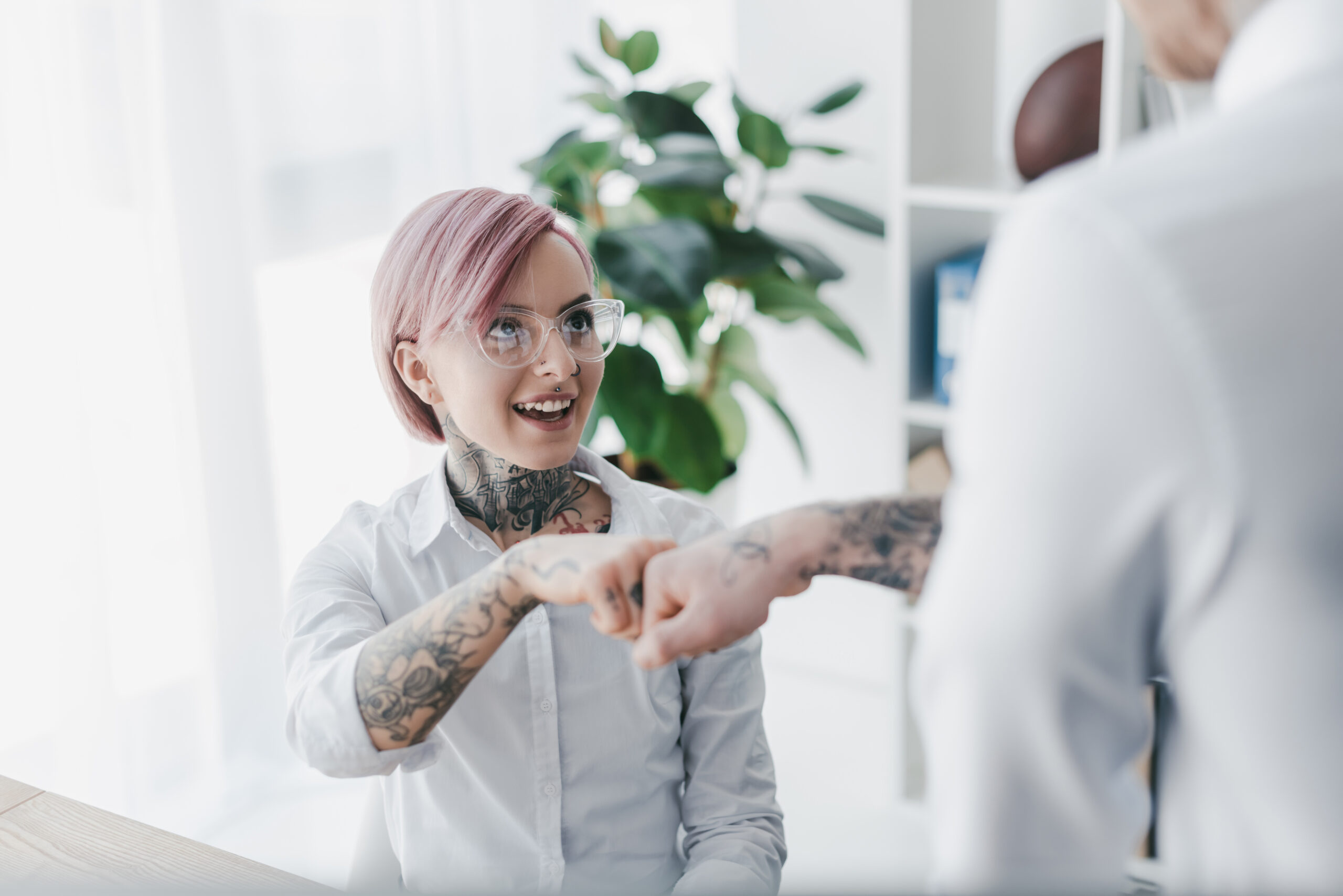 Young professionals with tattoos greeting with fist bump in modern office environment.