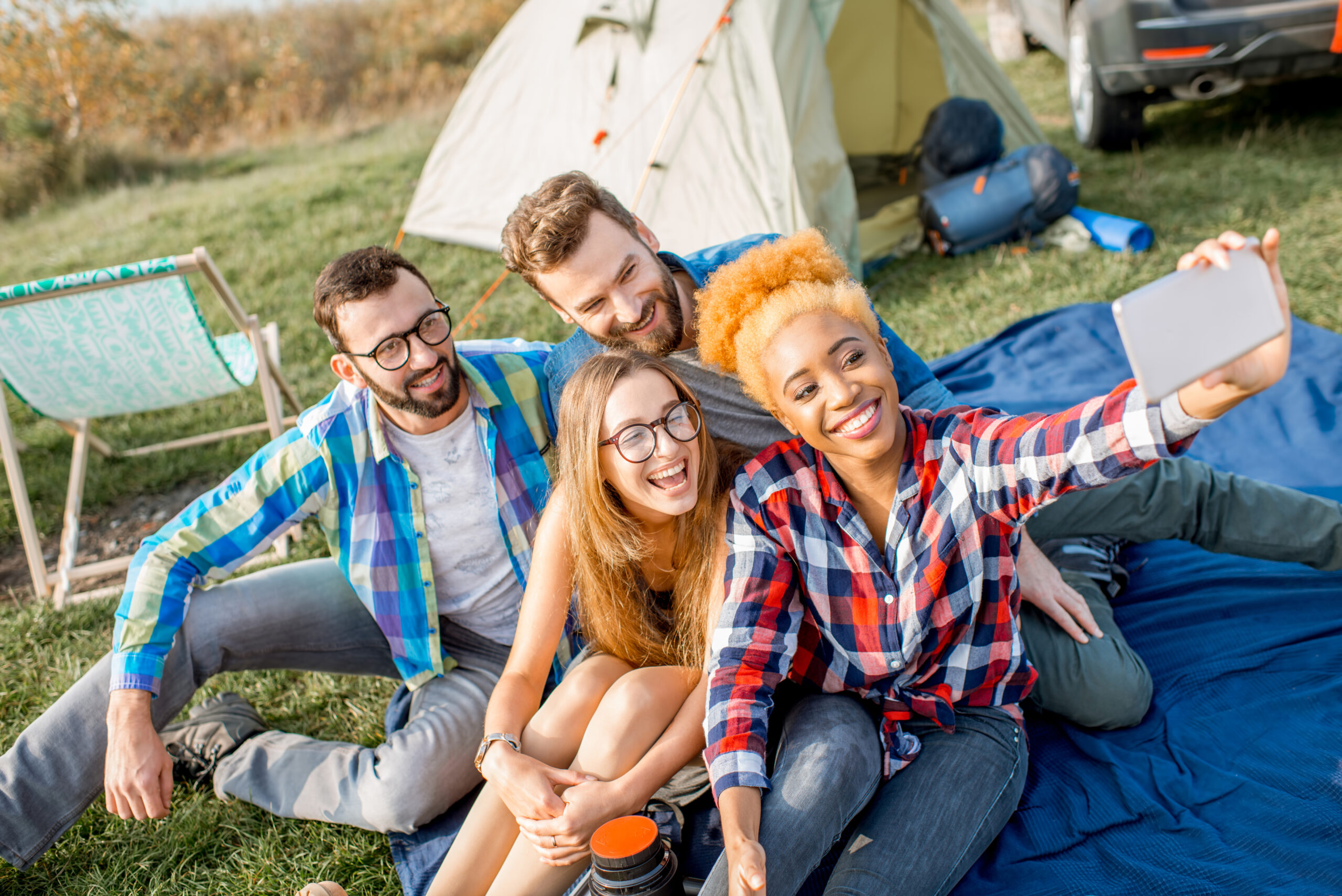 Four friends smiling together at camping site with tents and outdoor recreation gear.