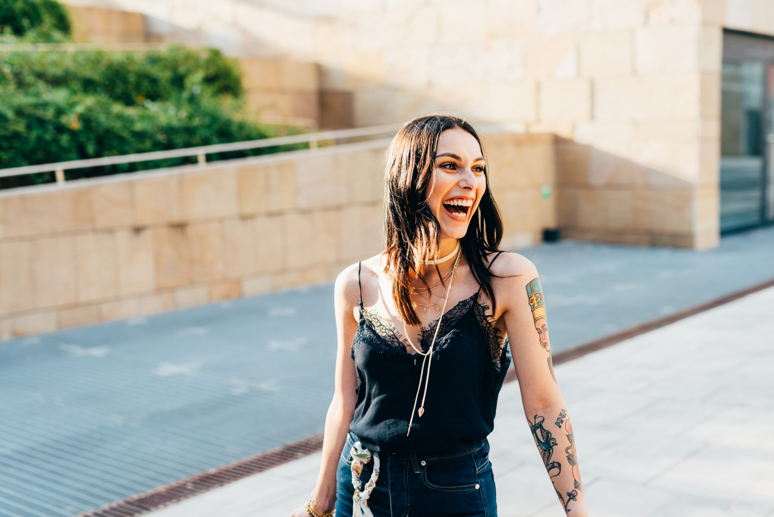 Young woman laughing outdoors in urban setting, expressing joy and happiness.