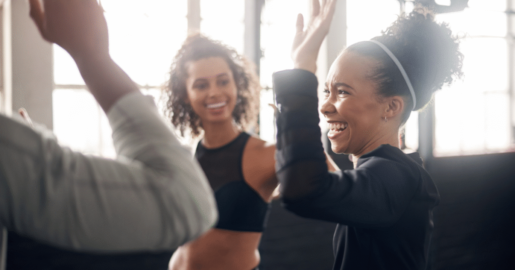 People smiling and raising their hands together in a supportive group setting, representing connection and encouragement for New Year&rsquo;s resolutions in addiction recovery.