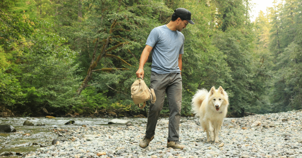 Person walking with a dog along a peaceful river, practicing healthy coping skills and self-care in addiction recovery.