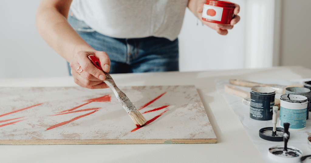 A person painting abstract red lines on canvas, using creative expression as a healthy distraction and coping skill in substance use recovery.