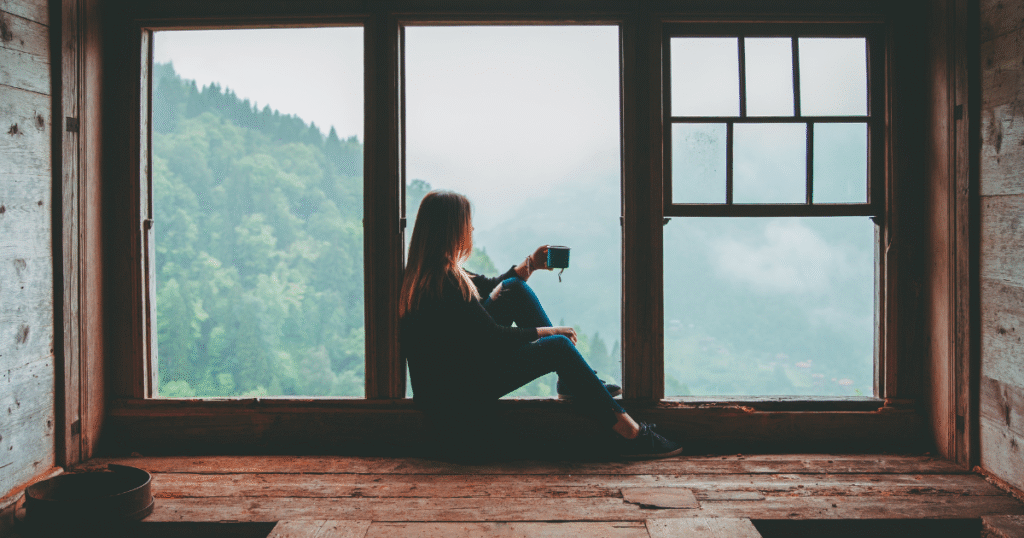 A person sitting by a window with coffee, symbolizing mindfulness and emotional awareness - key coping skills in recognizing early signs of cravings during recovery.