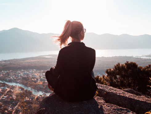 A woman on top of a hill, overlooking a view of a mountain and some land.