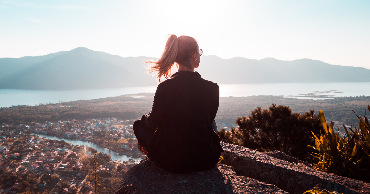 A woman on top of a hill, overlooking a view of a mountain and some land.