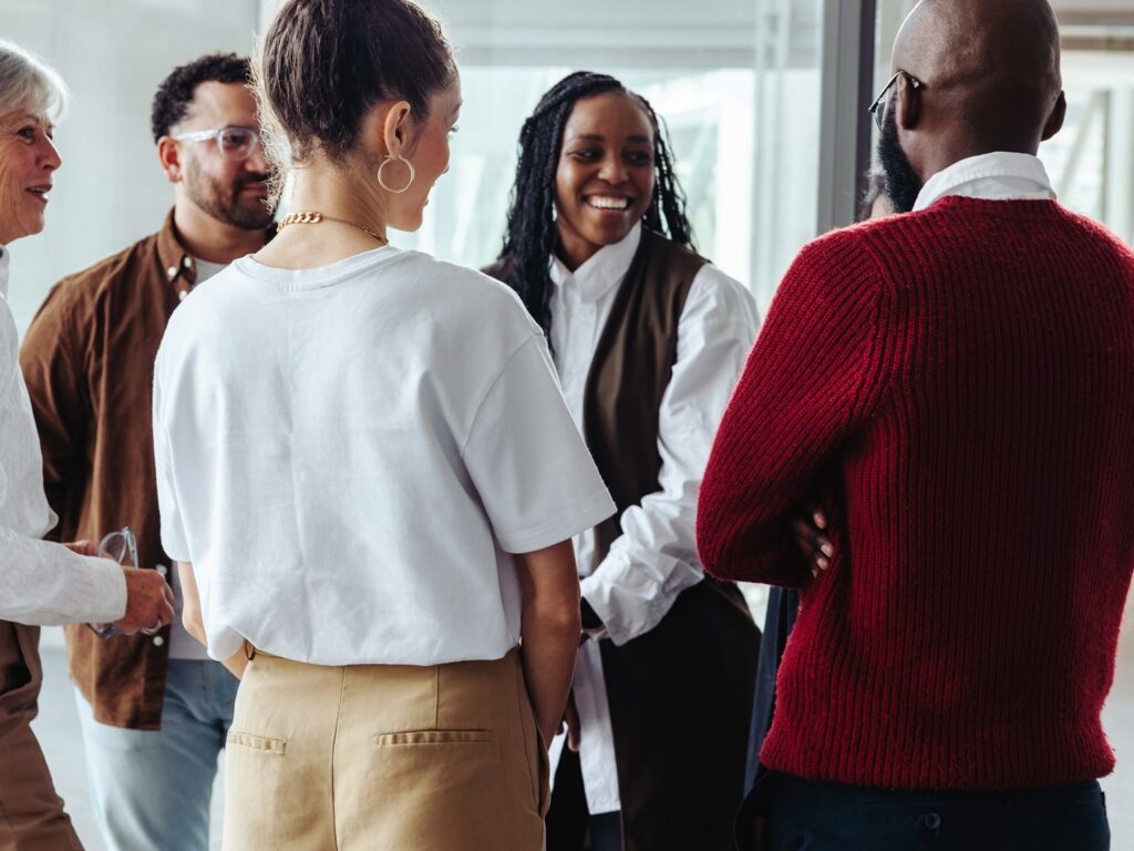 Diverse group of professionals engaged in friendly conversation in bright office setting.