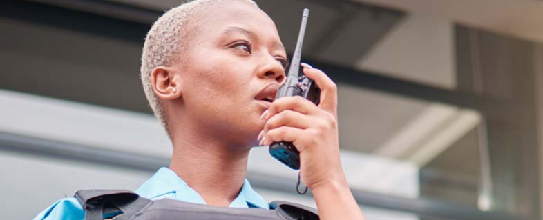Law enforcement officer speaking into radio communication device outdoors.
