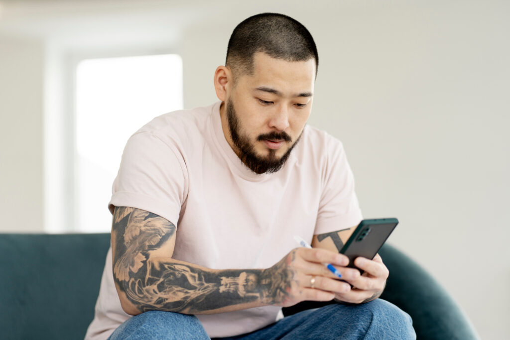 Man sitting on a couch on his phone learning about the upcoming Medicaid changes to stay informed about how it could affect substance use disorder treatment.